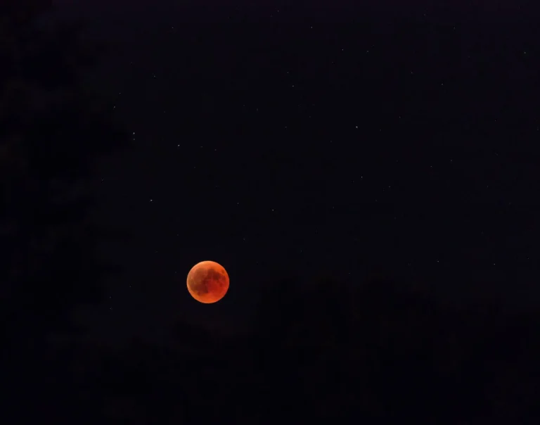 Fotografía creativa de un eclipse lunar del 7 de septiembre de 2025 con la Luna roja al fondo y una taza esmaltada de Monkey’s Coffee en primer plano, humeante, representando la unión entre la magia del cielo nocturno y el ritual de tomar café de especialidad.